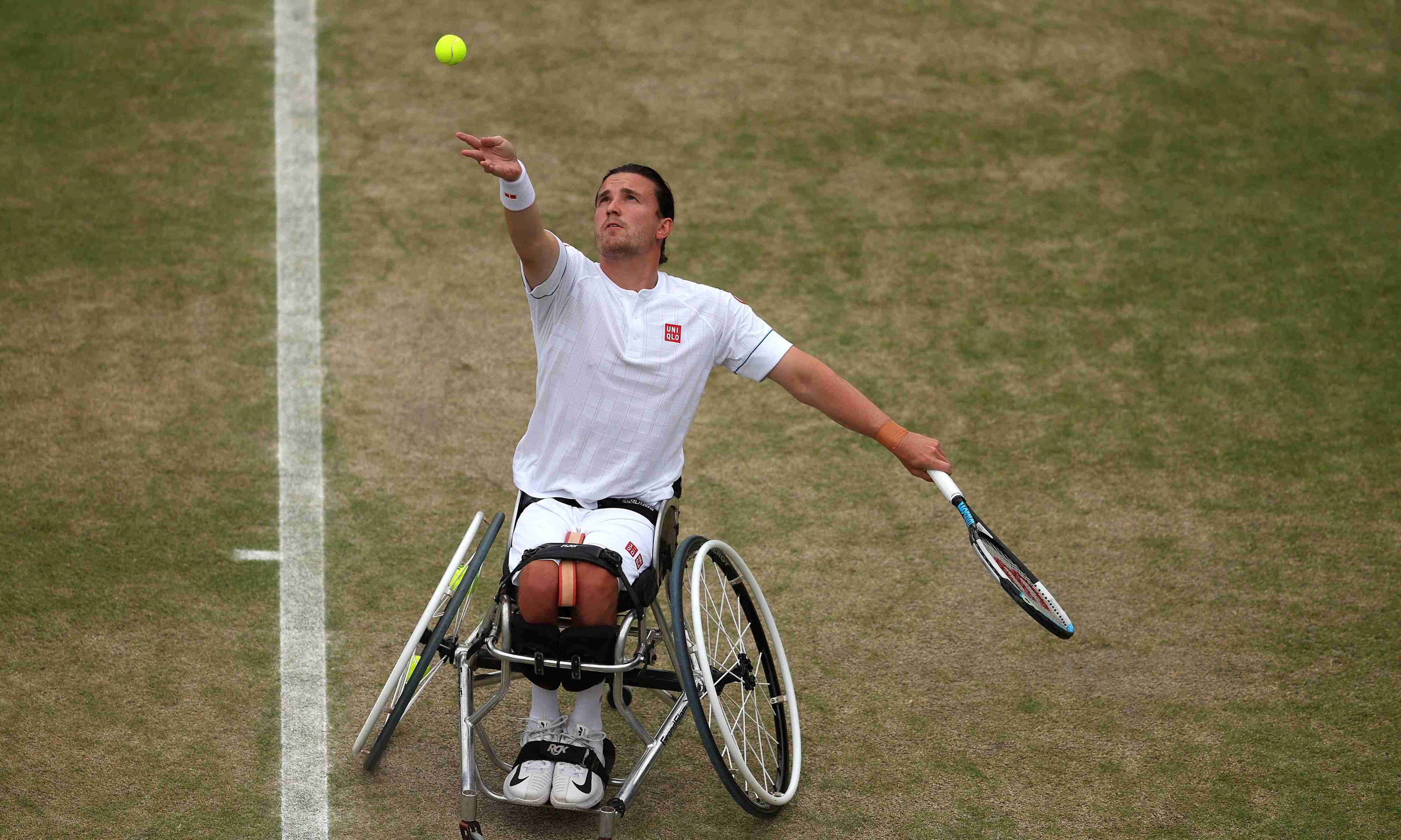 Wheelchair tennis player Gordon Reid throws tennis ball in the air and prepares to hit a serve on a grass court