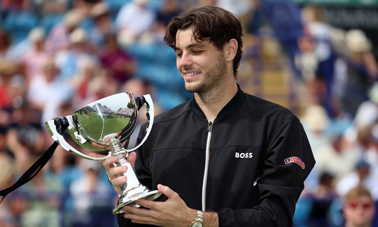 Taylor Fritz smiling and looking down at his trophy on court at the Rothesay International Eastbourne